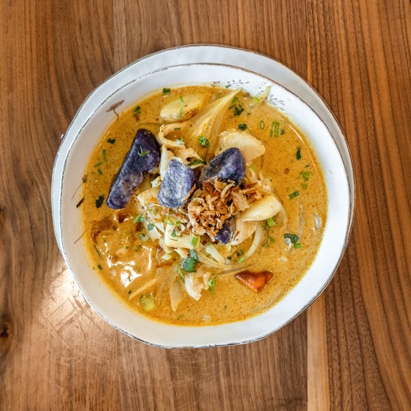 Overhead view of a bowl of yellow curry with purple potatoes, chicken, and fried onions.