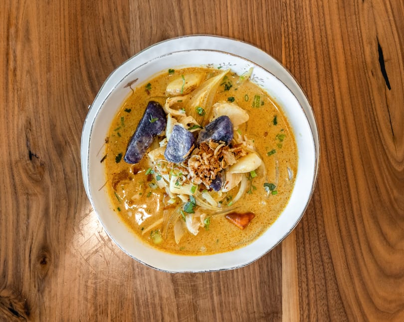 Overhead view of a bowl of yellow curry with purple potatoes, chicken, and fried onions.