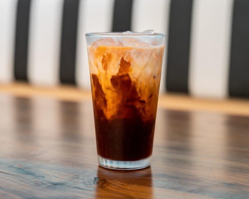 Iced Thai tea with milk swirling into the dark tea, on a wooden table.