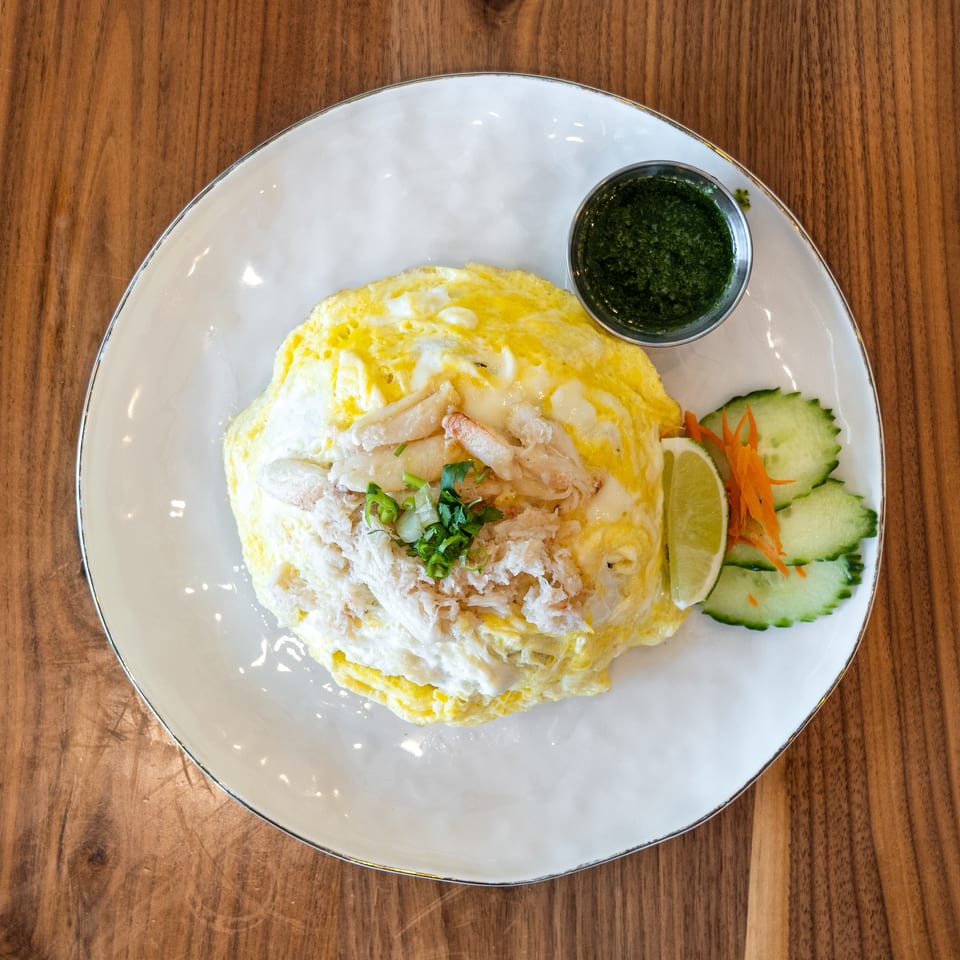Crab omelet with green sauce, lime, and cucumber slices on a white plate, on a wooden table.
