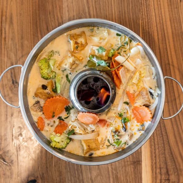Overhead view of a hot pot with a creamy broth, vegetables, tofu, and a flame in the center.