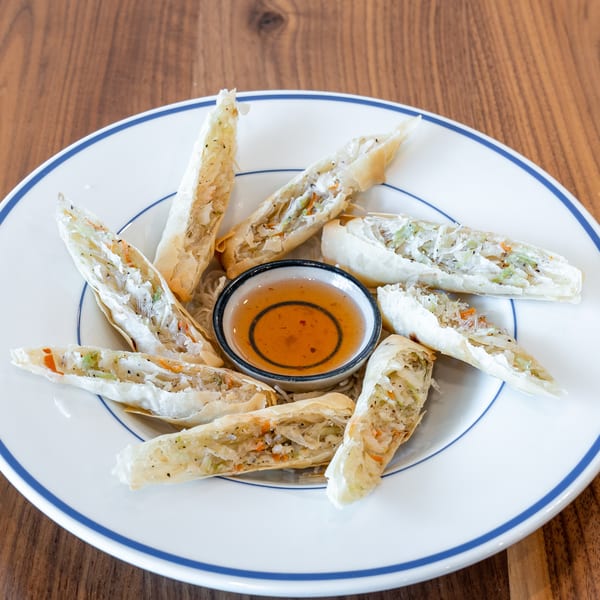 Crispy spring rolls filled with vegetables and noodles, arranged around a sweet chili dipping sauce.