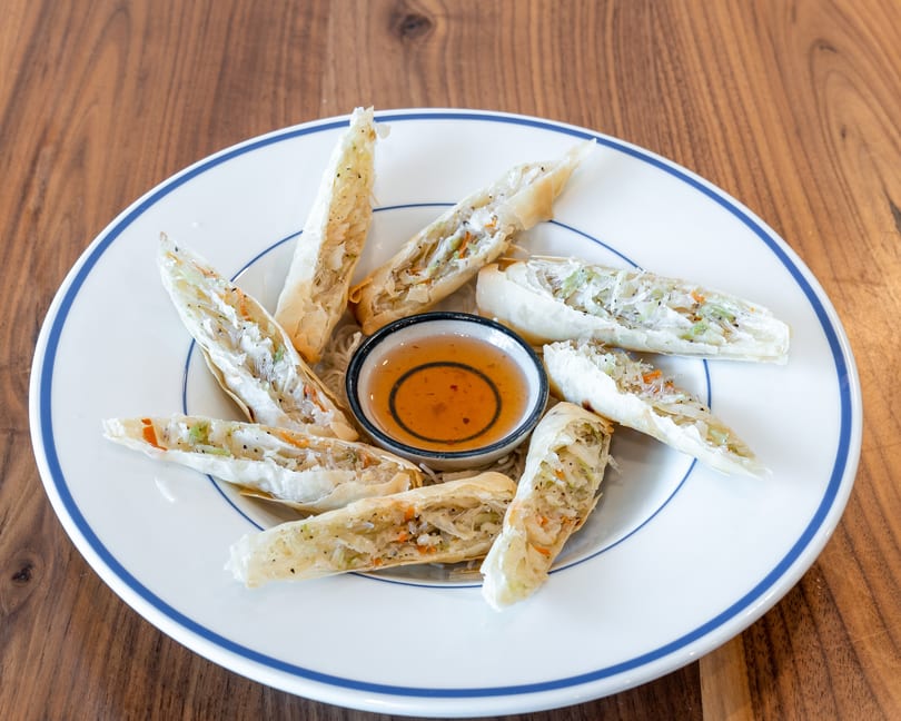 Crispy spring rolls filled with vegetables and noodles, arranged around a sweet chili dipping sauce.
