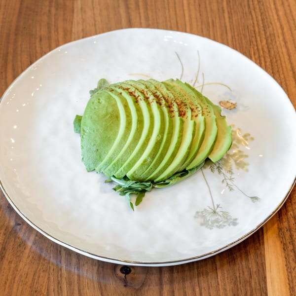 Sliced avocado with paprika and greens on a white plate with gold rim, on a wooden table.