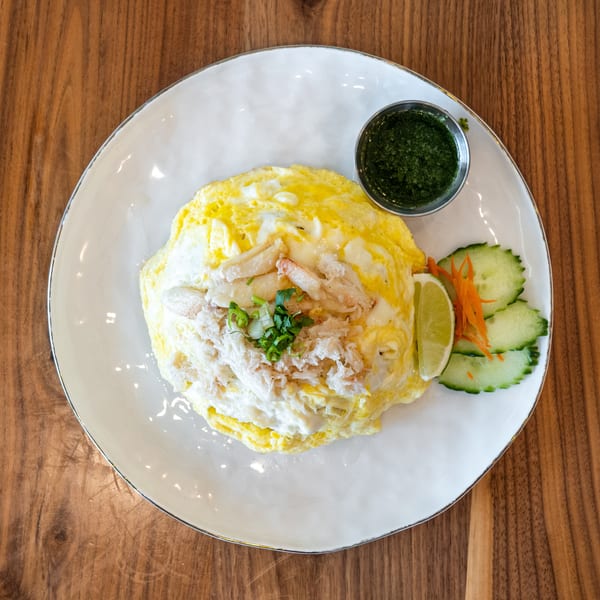 Crab omelet with green sauce, lime, and cucumber slices on a white plate, on a wooden table.