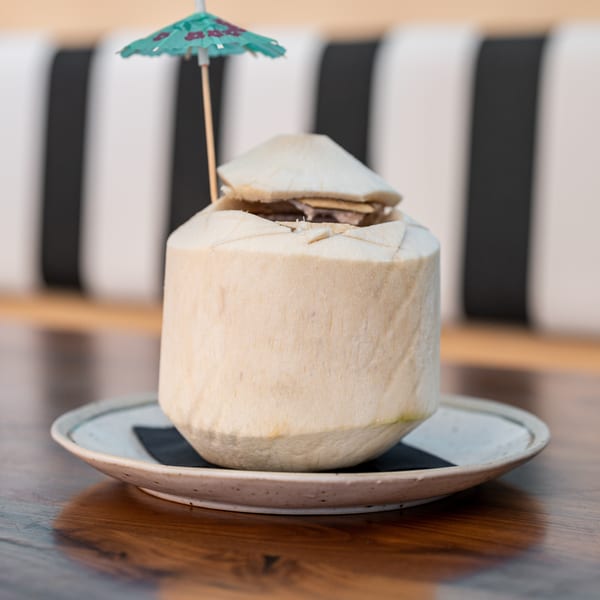 Fresh coconut drink with a small umbrella on a plate, on a wooden table.