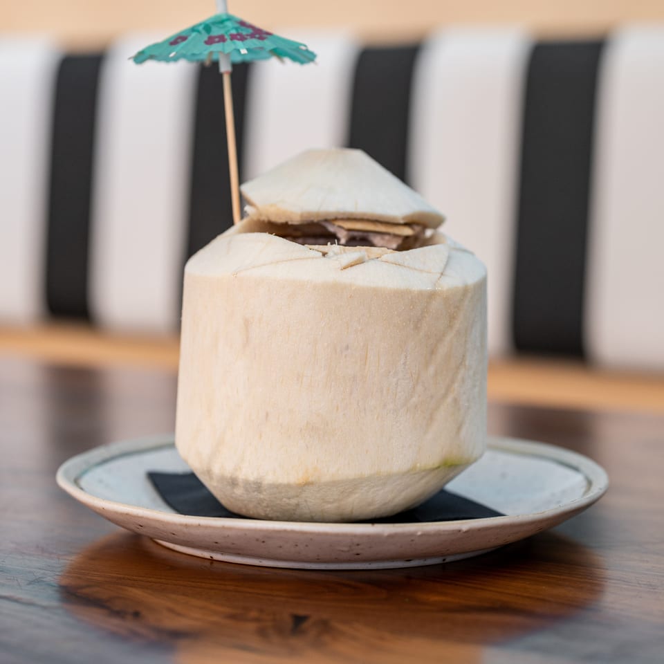 Fresh coconut drink with a small umbrella on a plate, on a wooden table.