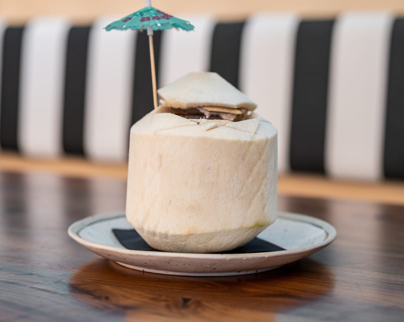 Fresh coconut drink with a small umbrella on a plate, on a wooden table.