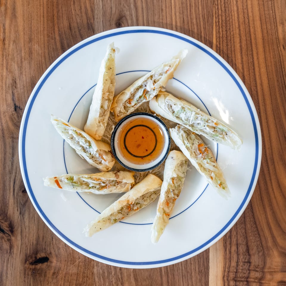Crispy spring rolls with vegetable filling and a side of dipping sauce on a white plate.
