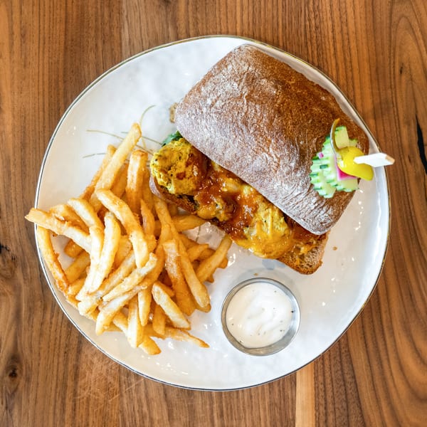 Top-down view of a sandwich with fries and dipping sauce on a white plate.