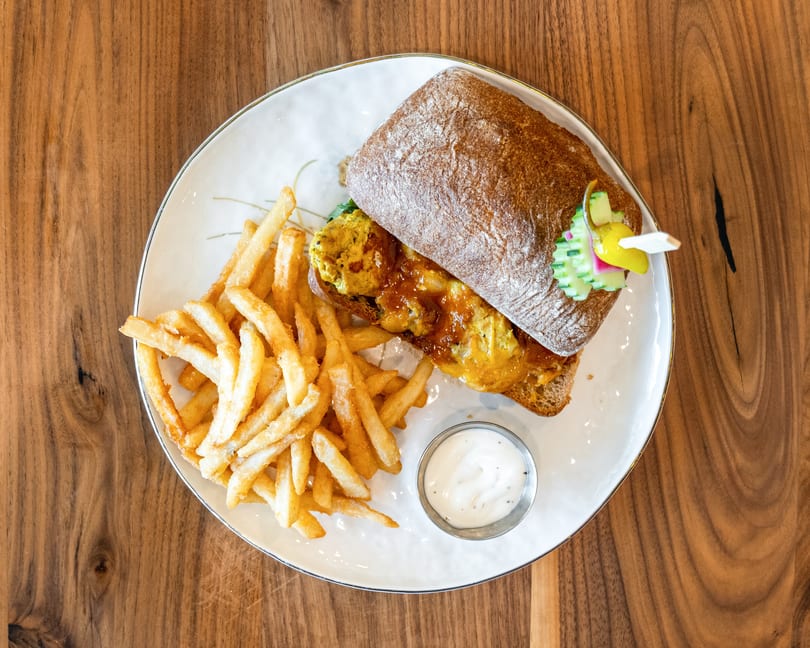 Top-down view of a sandwich with fries and dipping sauce on a white plate.