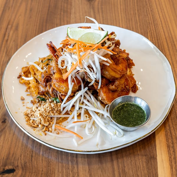 Shrimp Pad Thai with bean sprouts, shredded carrots, crushed peanuts, lime, and green sauce.