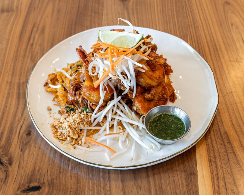 Shrimp Pad Thai with bean sprouts, shredded carrots, crushed peanuts, lime, and green sauce.